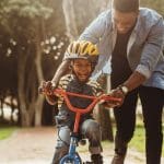 A father helping his son ride a bike.